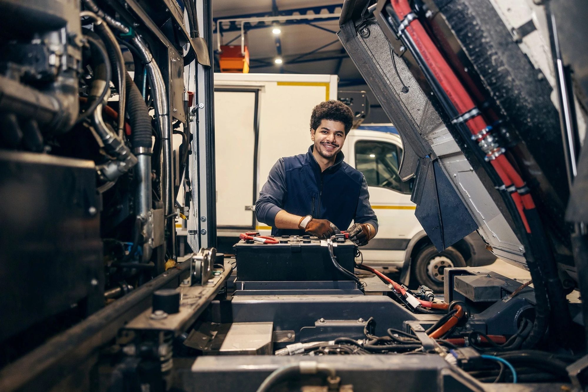 A technician working inside the open engine bay of a bus