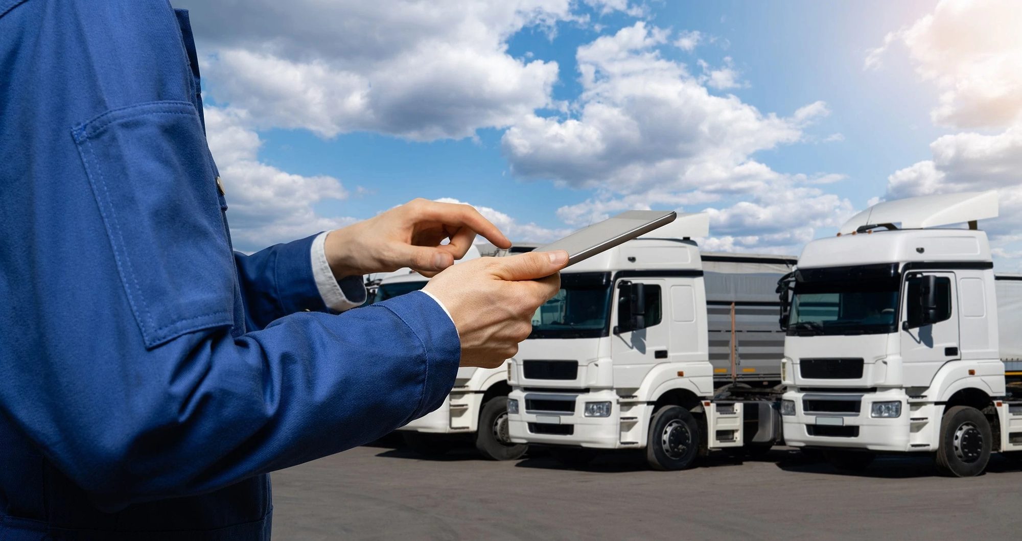 Hands in workshop overalls holding a tablet in front of two white trucks