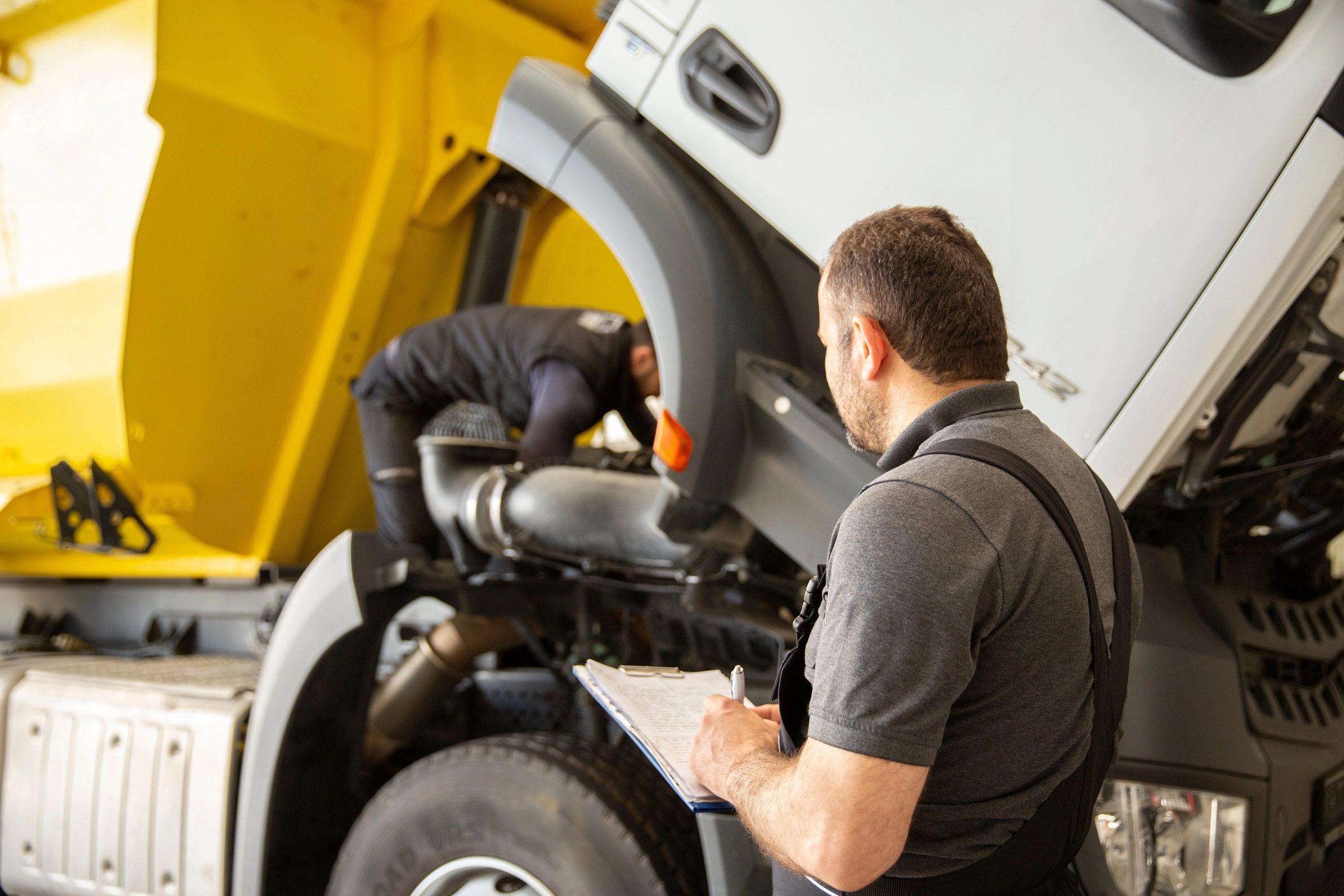Two technicians working under the raised bonnet of a heavy truck